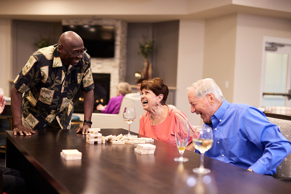 Seniors laughing together and playing a game at Croasdaile Village, a senior living community near Cary, NC.